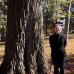 Woman with hands behind her back standing at a tall tree