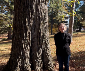 Woman with hands behind her back standing at a tall tree