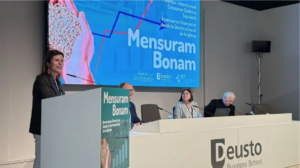 Woman standing at podium, with 3 panelists sitting to the left of her